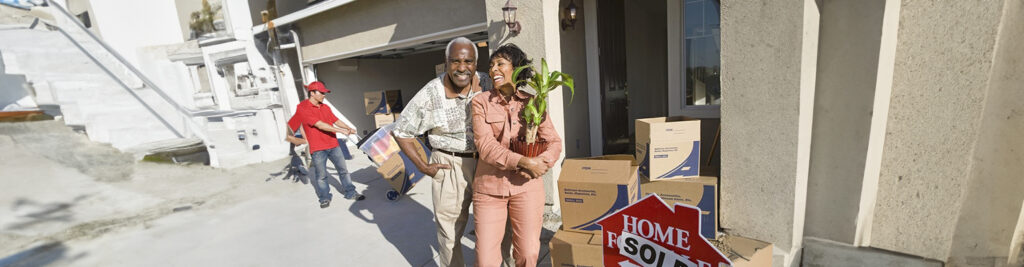 Senior couple carrying a plant and boxes out of their sold home