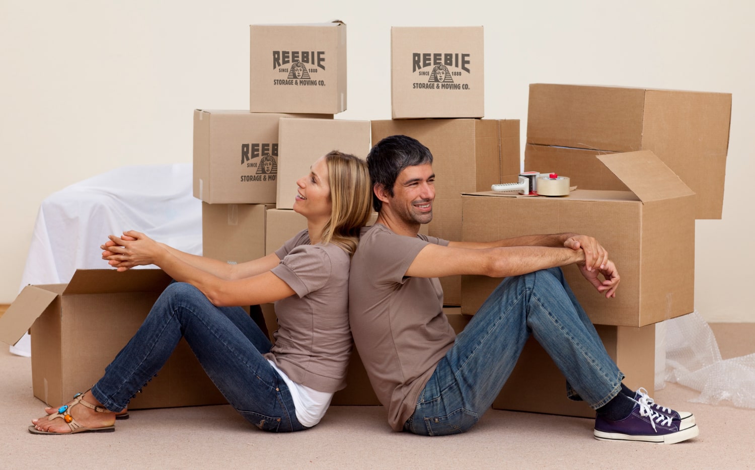 Couple sitting back to back among Reebie moving boxes