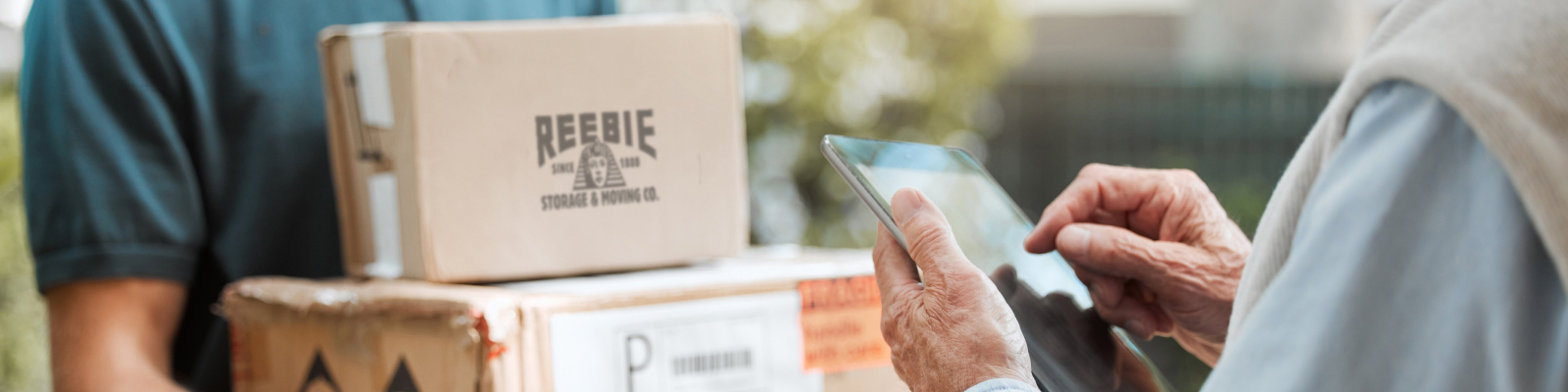 Mover holding a Reebie box and checking a tablet with a customer