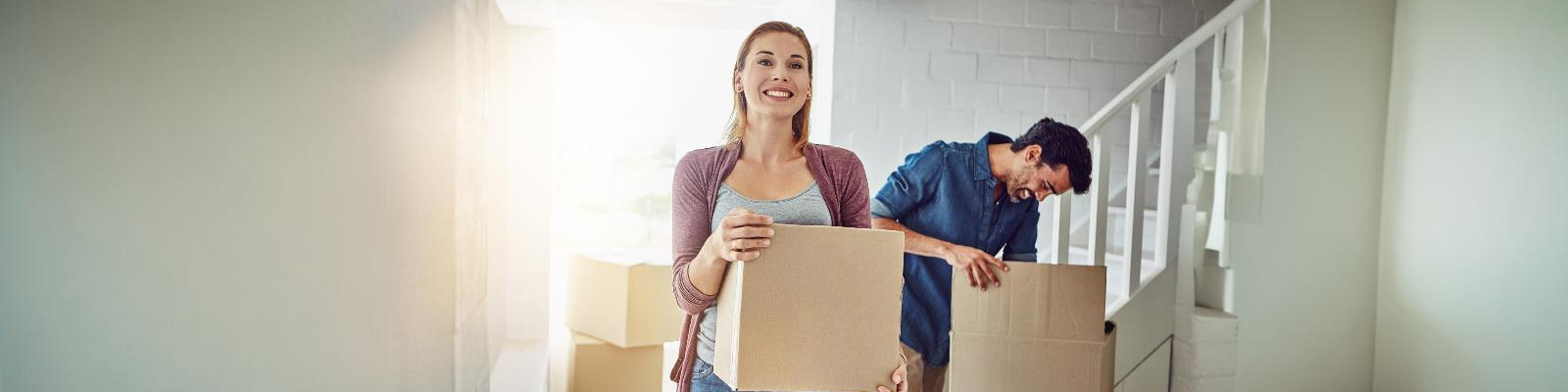 Couple carrying a box up the stairs of a bright home