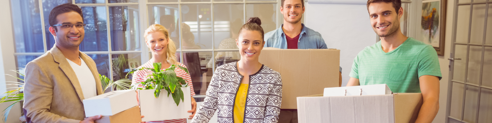 Group of coworkers holding plants and boxes during an office move