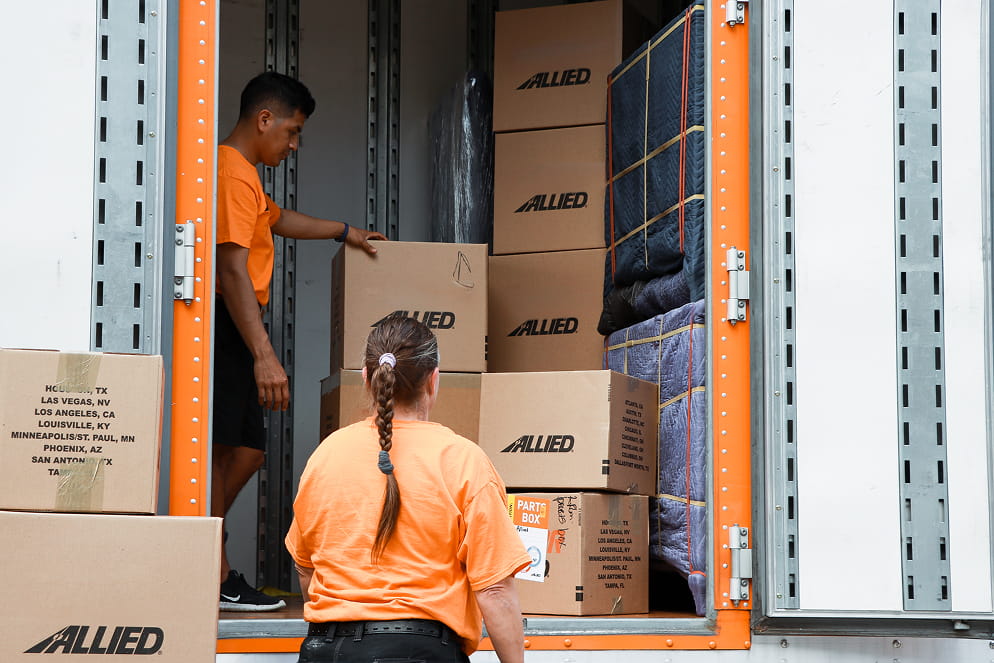 Two movers loading boxes and blankets into an Allied truck