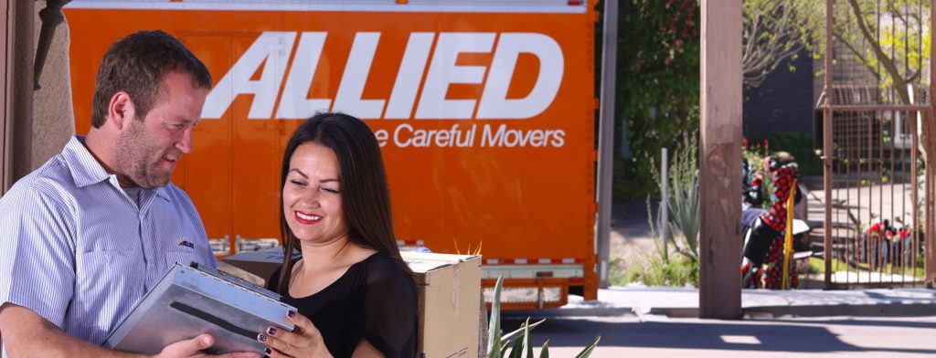Allied mover showing a woman a tablet in front of an orange truck